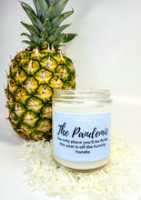 Load image into Gallery viewer, There is a highly scented soy candle called The Pandemic that is sitting on a mound of shaved coconut. Behind it stands a fresh pinapple.