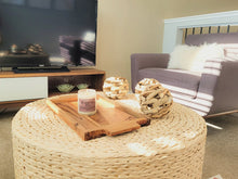 Load image into Gallery viewer, The Work From Home candle is sitting on a wicker table on a serving tray in a living room with a television, a television stand, and a comfy chair in a living room