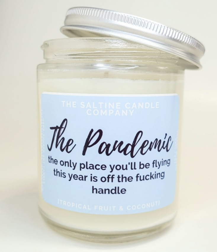 The Pandemic candle has a pastel blue label and says The Saltine Candle Company. The description on it says the only place you'll be flying this year is off the fucking handle. It says it smells like tropical fruit and coconut. 